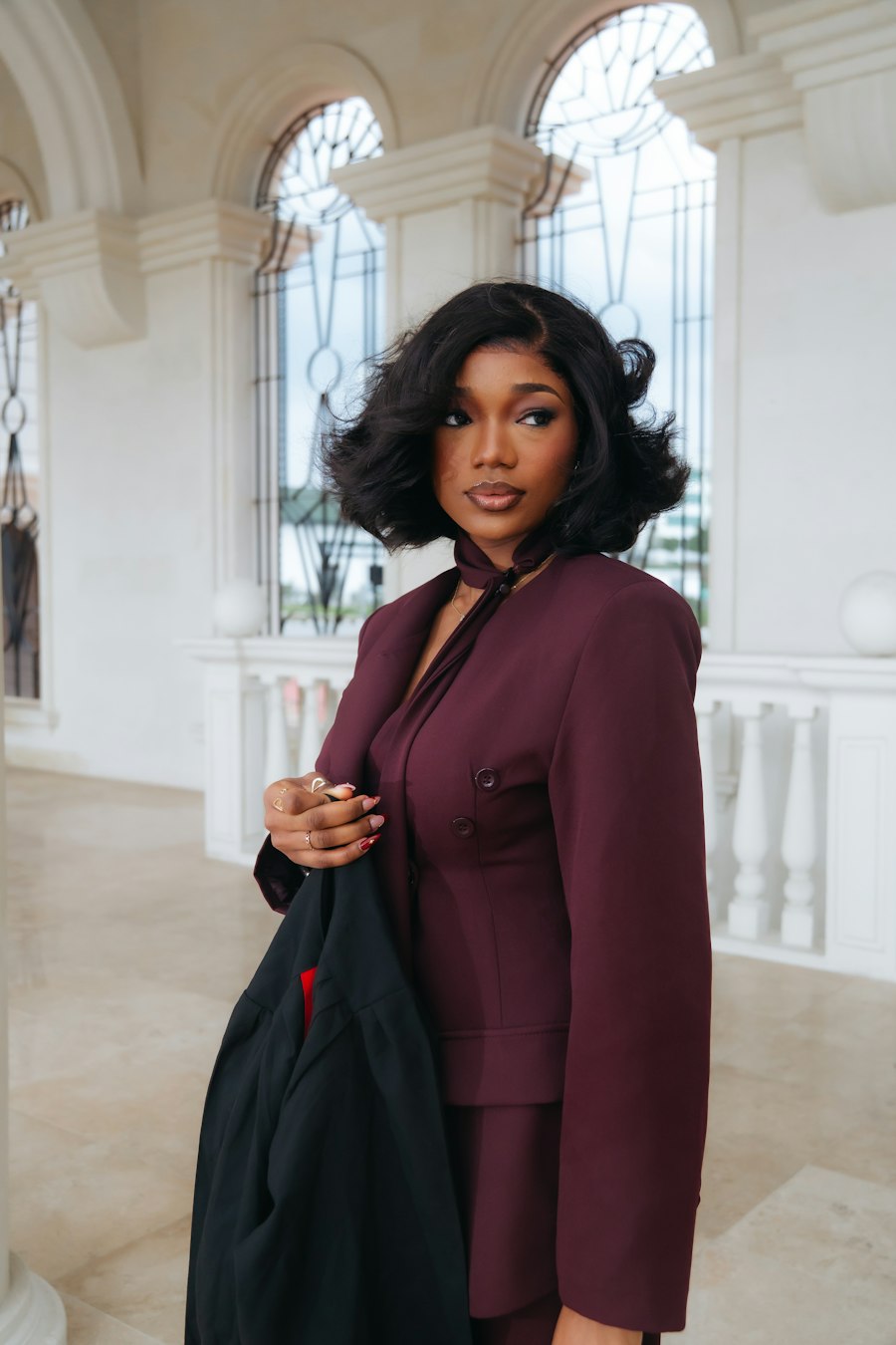 Odile in a burgundy suit in a sunlit hall
